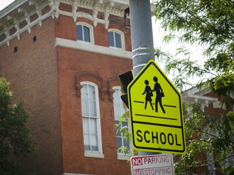 A neon yellow 'children crossing road sign' on a street pole in front of a red brick building.