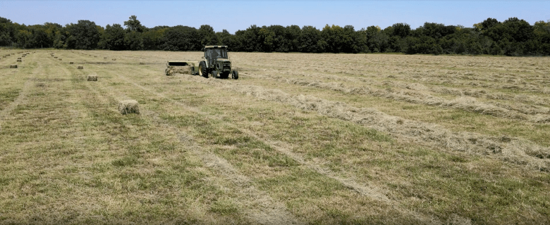 A green tractor picks up hay on a sprawling farm.
