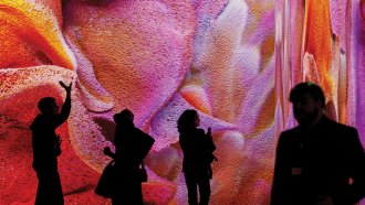 A photograph of four silhouetted people standing in front of a warm toned abstract piece of artwork that featured tones of yellow, red, orange and pink swirls.
