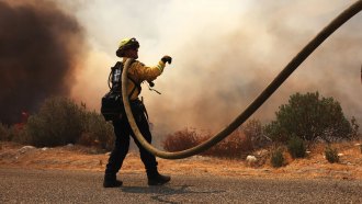 A photograph of a male firefigther with a hose works at a back burn during the Fairview Fire in Southern California in September 2022