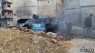 A man walks past a smouldering police armoured vehicle in Homs (6 February 2012)