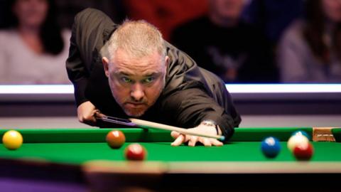 Stephen Hendry leans over a snooker table with a snooker cue in his hand