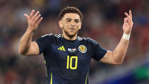 Scotland striker Che Adams holds his arms up during a Euro 2024 match
