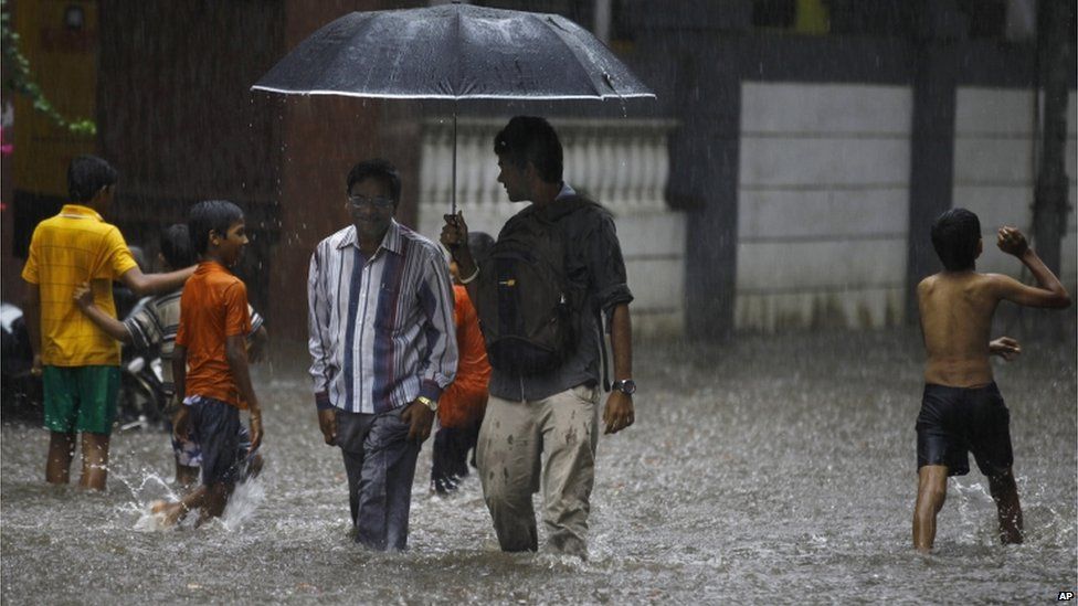 Children play as two men walk through a flooded street during monsoon rains in Mumbai, India, Sunday, June 9, 2013. The Southwest monsoon, arrived in the city Saturday, three days ahead of schedule, according to the meteorological department