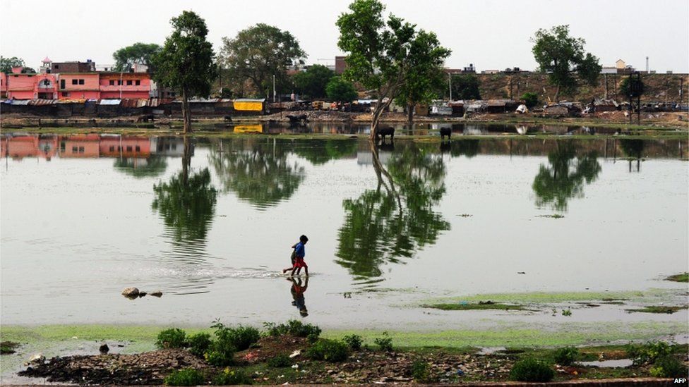 Indian children wade through a submerged area after a rain shower in Allahabad on June 9, 2013