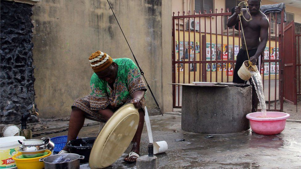 A Nigerian man fetches water from a well as a woman washes the dishes in Lagos on 19 March 2015