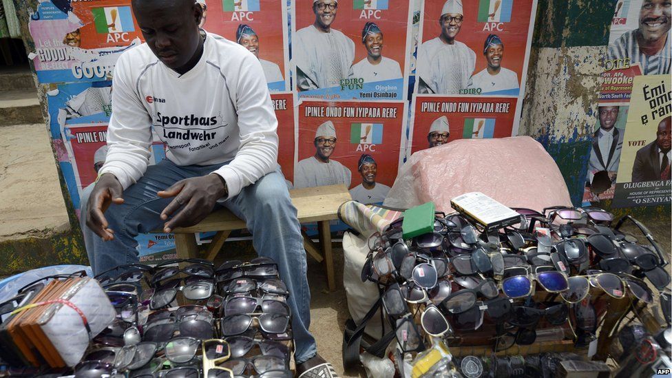 A vendor sells sunglasses at his roadside shop in front of posters of the main opposition All Progressives Congress (APC) presidential candidate Mohammadu Buhari and running mate Yemi Osinbajo in downtown Akure, Ondo State south-western Nigeria, on 23 March 2015