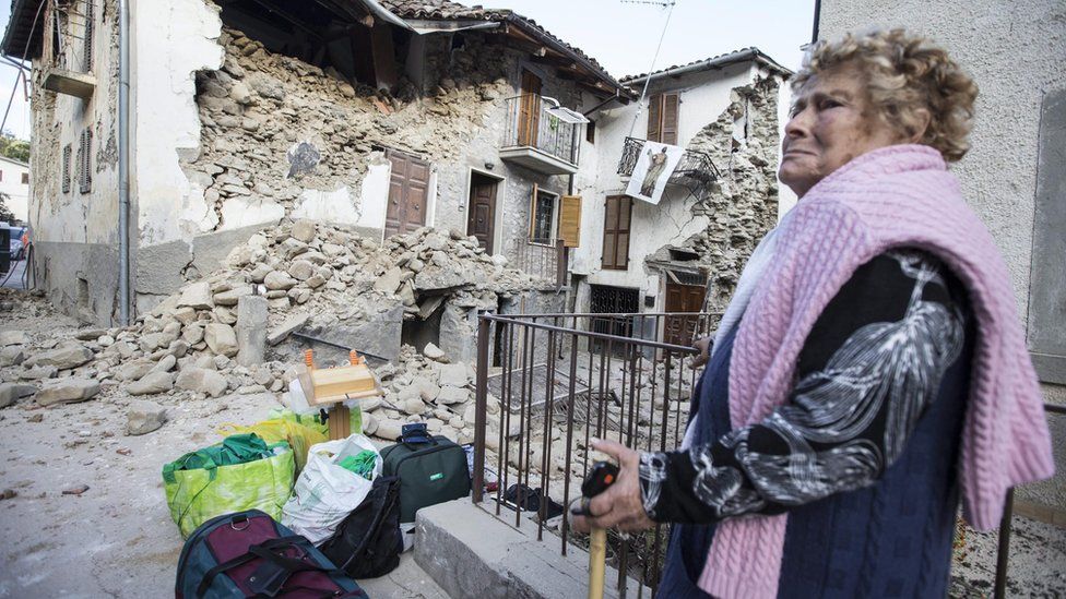Woman stands next to rubble in Accumoli