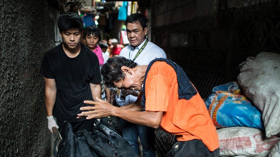 This picture taken on 1 September 2016, shows the grieving father of a suspected drug user killed by the police in Manila, as another man wheels the body away in a bag.