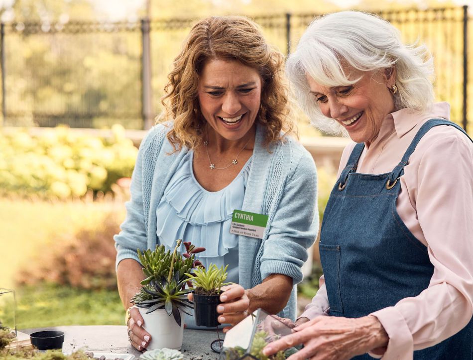 Senior women and Atria employee smiling while potting plants outdoors.