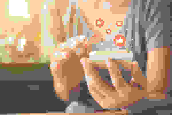 A hand holding a phone and using it, along with orange digital illustrations of messaging bubbles, thumbs up, and a heart