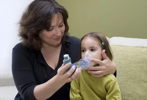 A mother helps her daughter with an asthma inhaler.