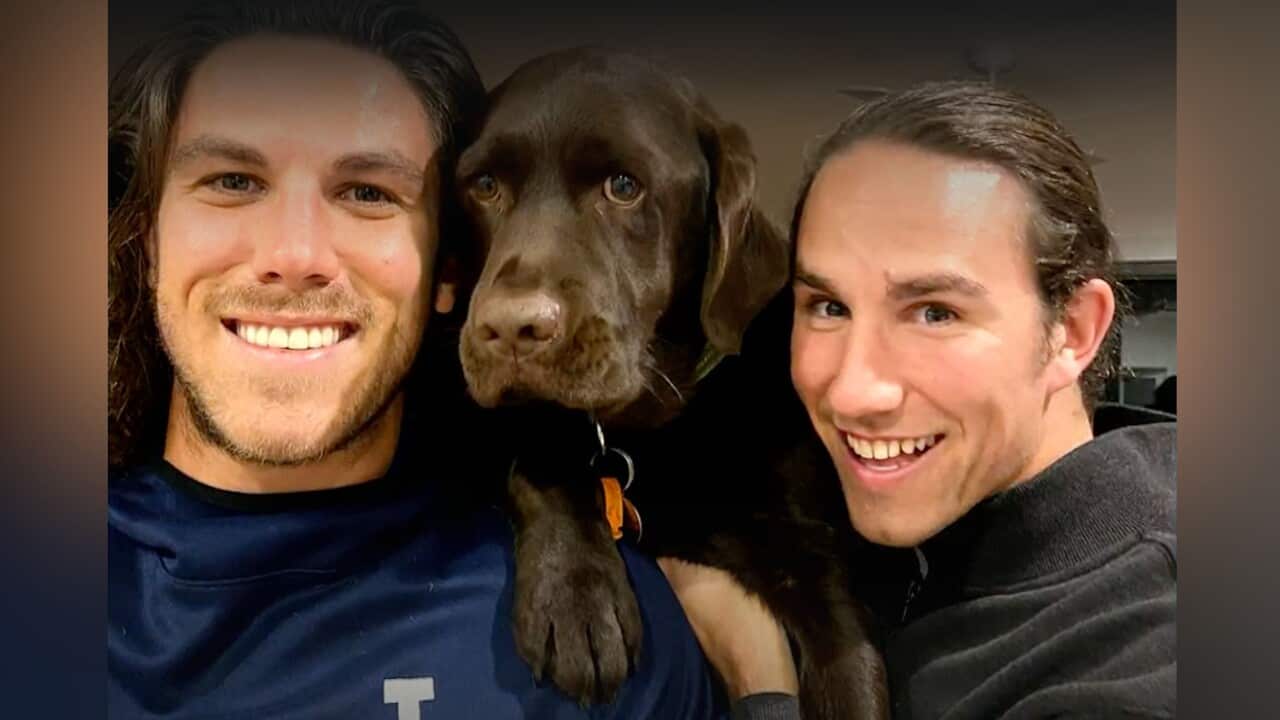 Two men with brown hair posing for a photo with a brown dog.