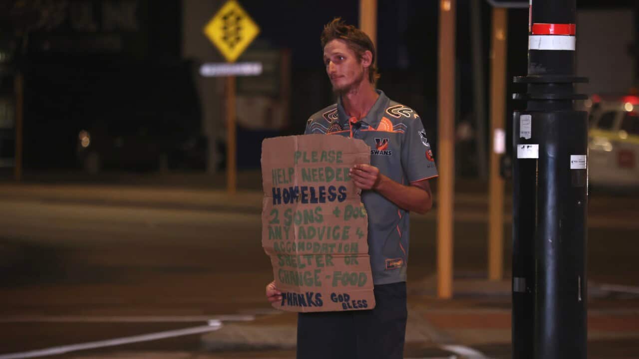 A middle-aged man holding up cardboard at a busy intersection, pleading for spare change