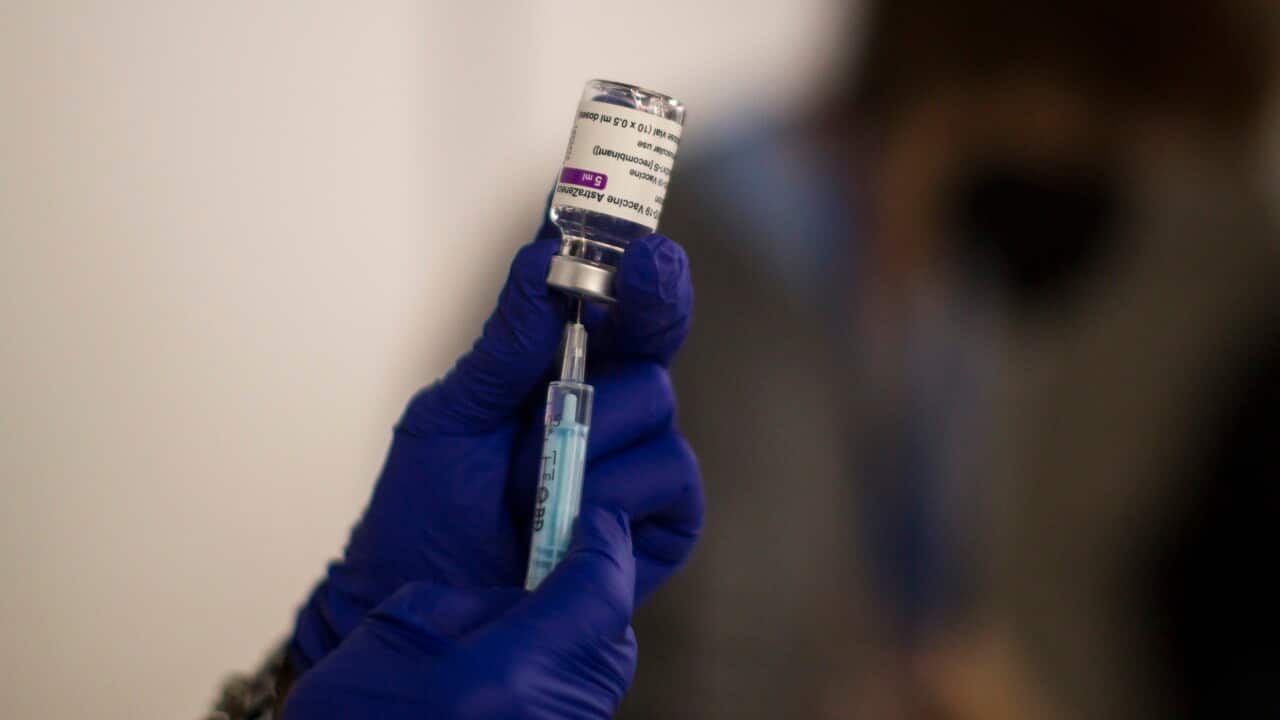 A gloved hand holding a vaccine being put into a needle.