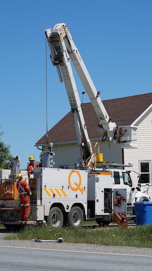 Deux travailleurs sur un camion d'Hydro-Québec stationné devant une maison.