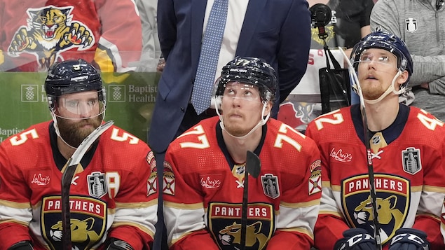Assis au banc de leur équipe, trois joueurs de hockey affichent un air dépité.