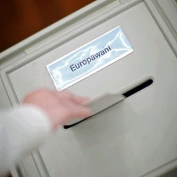 Eine Hand wirft einen Stimmzettel in den Schlitz einer Wahlurne mit der Aufschrift Europawahl