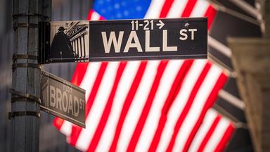 Wall Street Straßenschild vor einer amerikanischen Flagge.