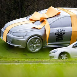 Eine Skulptur, die einen Volkswagen Golf zeigt, ist mit einer Schleife und der Aufschrift "50 Jahre Golf - Wolfsburg" zu sehen.
