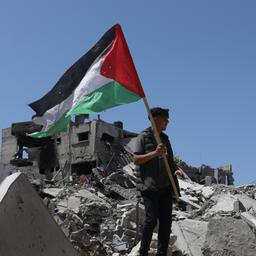 Ein Mann steht auf Trümmern und hält eine palästinensische Fahne in der Hand.