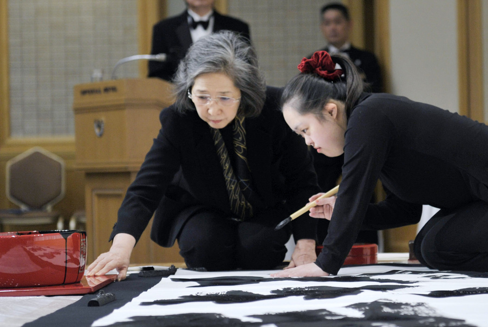 輪島塗の墨つぼなどを使って揮毫する金沢翔子さん（右）。見守るのは母泰子さん＝２０１５年１１月、東京都内