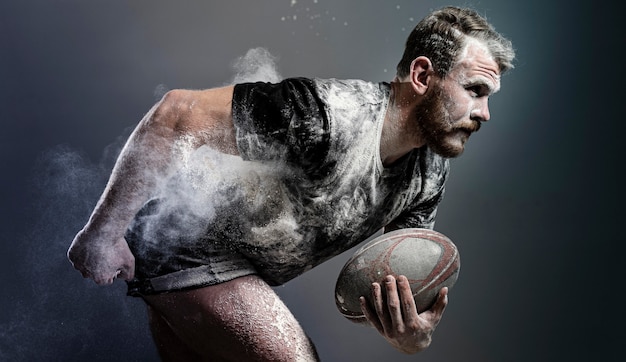 Vista laterale del giocatore di rugby maschile atletico che tiene palla con polvere