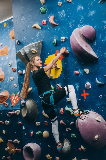 Giovane donna arrampicata su una parete di arrampicata su roccia alta, coperta, artificiale