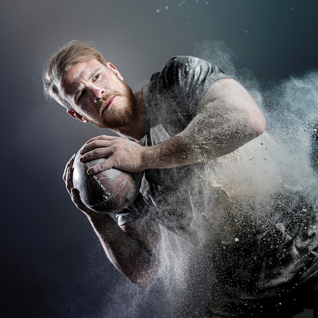 Giocatore di rugby maschile atletico che tiene palla con polvere