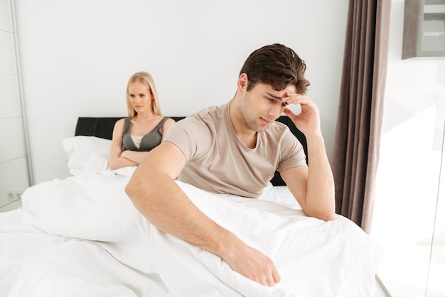 Upset man sitting with his sad woman in bed at home