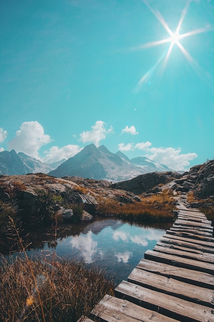 Free photo vertical shot of a wooden passage over a reflective small lake and a mountain range on the horizon