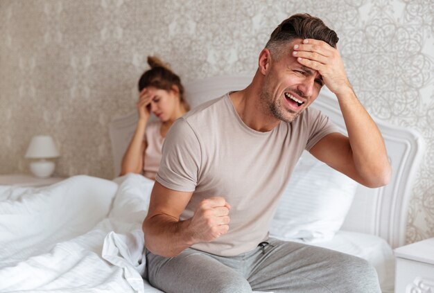 Confused worried man sitting on bed with his girlfriend