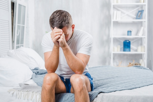 Frustrated man with headache sitting on bed at home