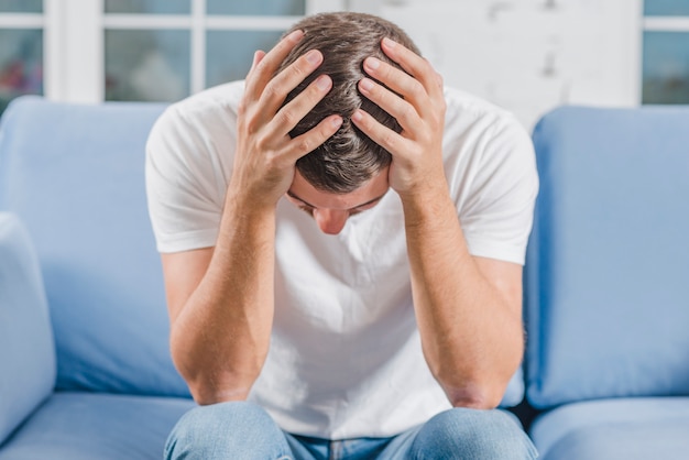 Frustrated man suffering from headache sitting on sofa