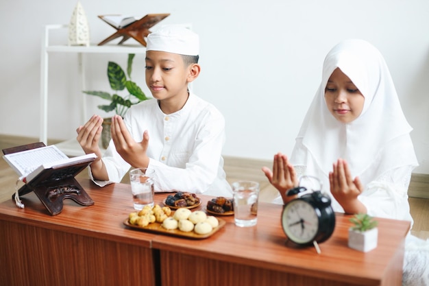 Young Muslim boy and girl praying while waiting for iftar in Ramadan