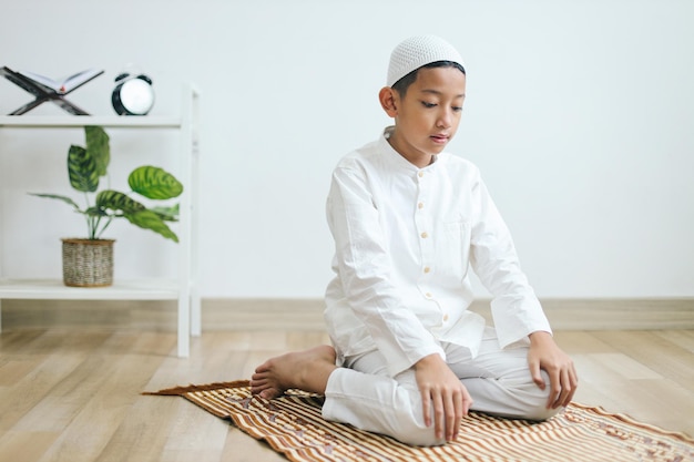 Young muslim boy praying on prayer mat and doing one of movement gesture in salat procedure