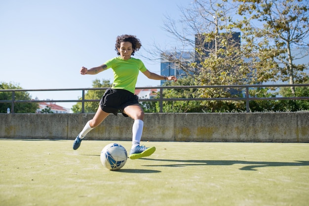Решительная молодая женщина, играющая в футбол. Спортсменка в яркой форме бегает по полю, пинает мяч. Спорт, отдых, концепция активного образа жизни