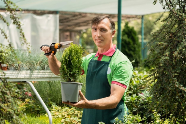 Фото Зрелый мужчина работает в садовом центре, стоя и держа растения в горшке.