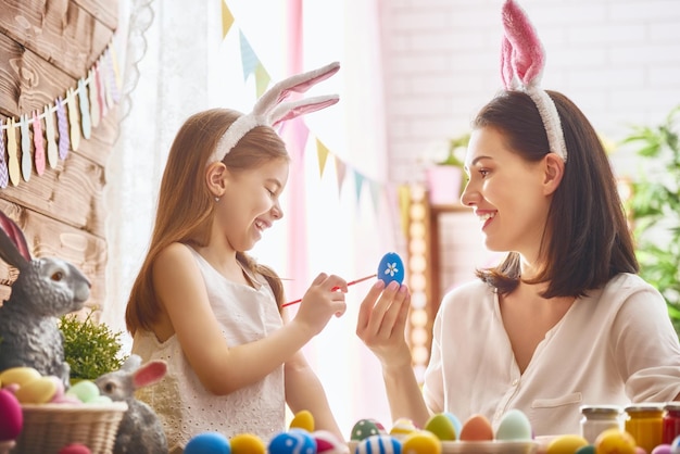 Mother and her daughter painting eggs Happy family preparing for Easter