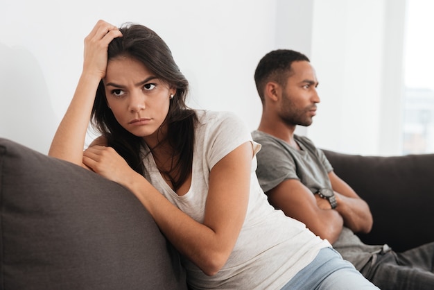 Picture of young sad couple quarreling while sitting on sofa.