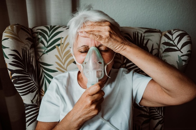 Senior woman wearing oxygen mask sitting on chair at home