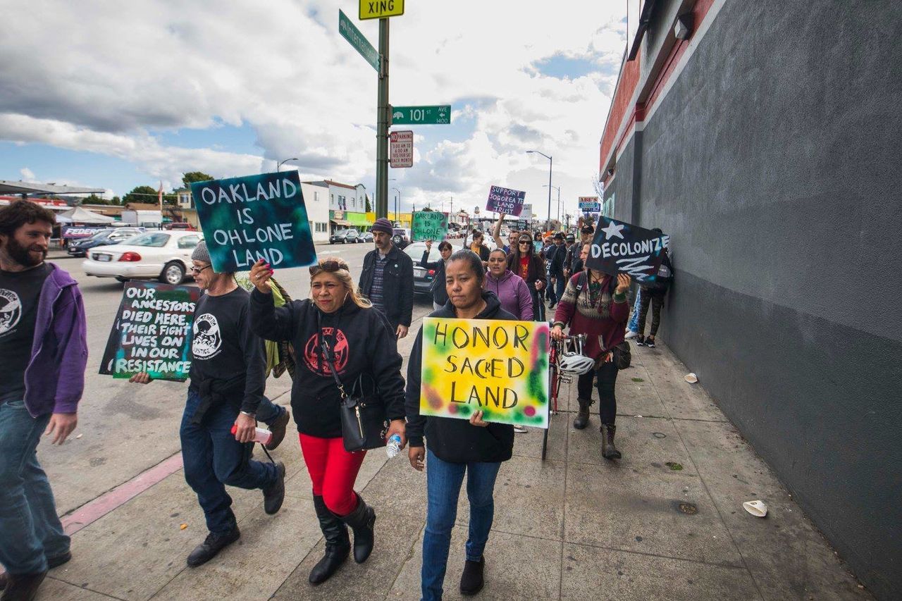 Advocates march with signs on the day of the land-honoring ceremony for the plot in Oakland.