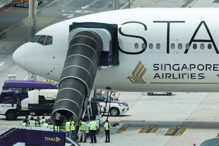 Airport employees gather on May 22, 2024, around an airstair attached to Singapore Airlines flight SQ321 as it stands parked on the tarmac Suvarnabhumi Airport in Bangkok, where it made an emergency landing after a severe, midair turbulence incident.




