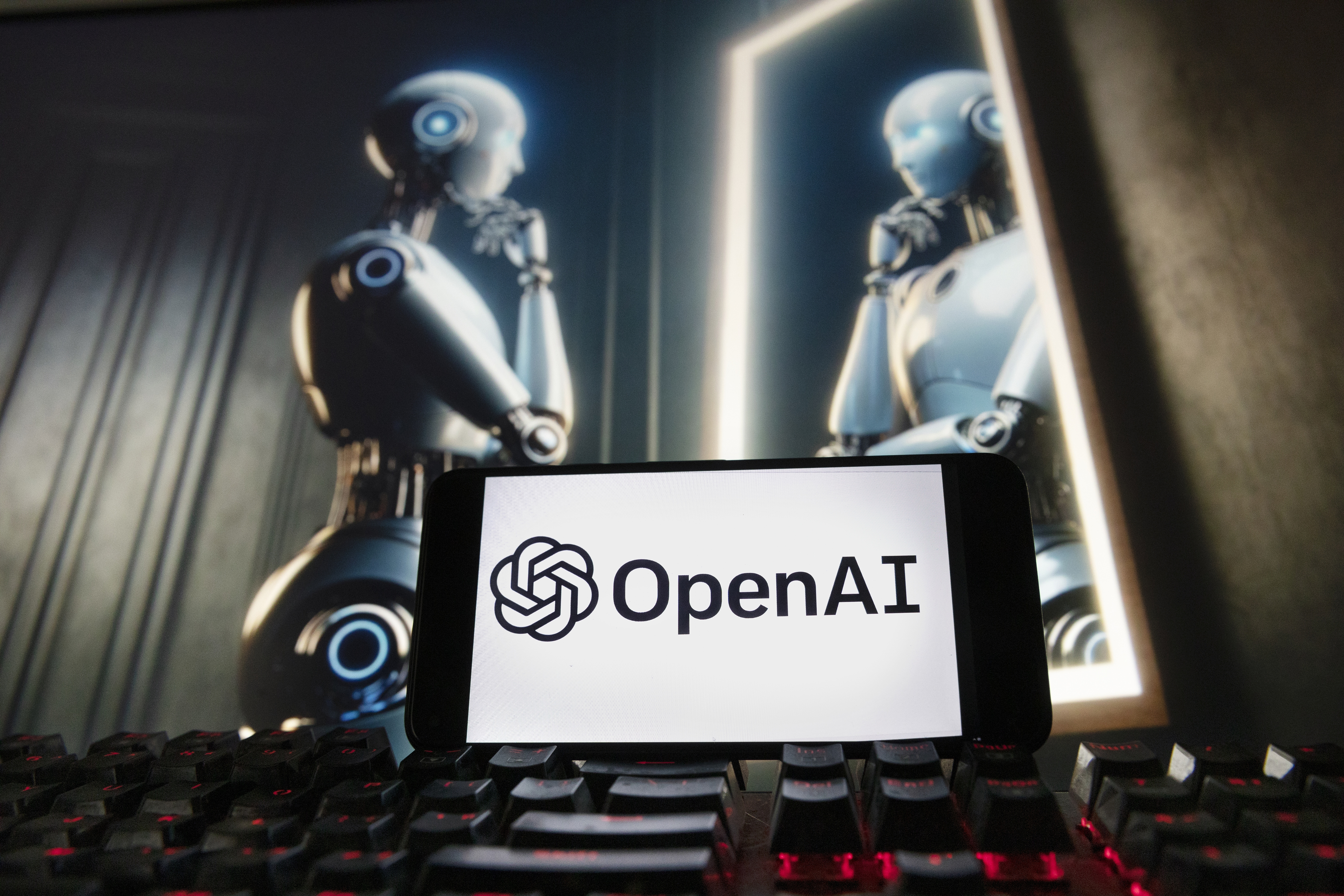 FILE- The OpenAI logo is displayed on a cell phone with an image on a computer monitor generated by ChatGPT's Dall-E text-to-image model, Dec. 8, 2023, in Boston. One of the original creators of the artificial intelligence technology behind ChatGPT says he is leaving the company after a nearly decade. OpenAI cofounder Ilya Sutskever announced his decision on the social media site X on Tuesday, May 14, 2024. Sutskever will be replaced by Jakub Pachocki as chief scientist at OpenAI. (AP Photo/Michael Dwyer, File)