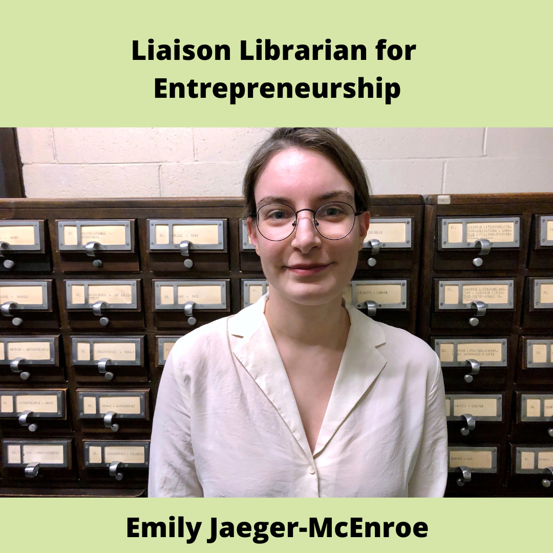 Liaison Librarian for Entrepreneurship Emily Jaeger-McEnroe, a younge brunette woman with glasses has a closed mouth smile, she is wearing a white button down shirt and is standing in front of a card catalogue.