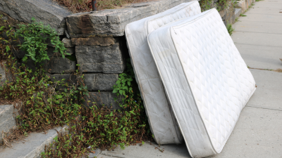 two old mattresses propped up on sidewalk outside