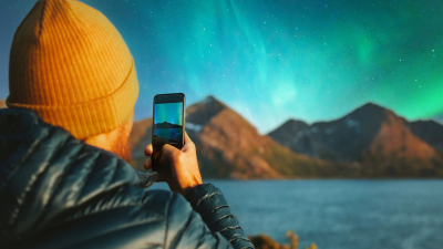 Man with smartphone taking photo of northern lights