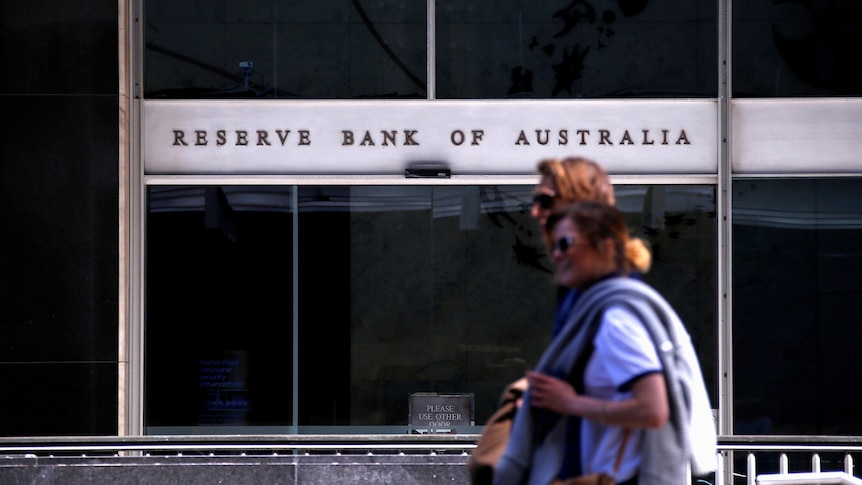 Two  women walk past the Reserve Bank of Australia headquarters, with the building's name prominent in the background.