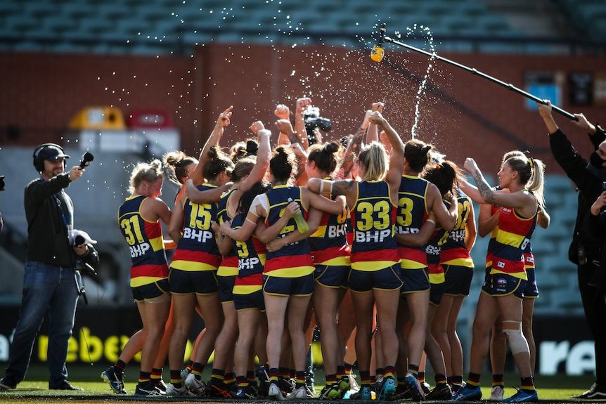 The whole Adelaide Crows team stand in a huddle and celebrate, squirting water everywhere