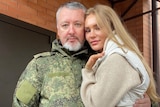 A man in camouflage gear puts his arm around a blonde woman 